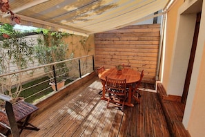A wooden deck with a round table and chairs, surrounded by potted plants and a metal bench. - Downtown Colmar, parking lot, terrace, air-conditioned, private parking (Colmar)
