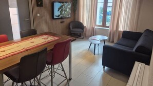Een moderne woonkamer met een houten eettafel, rode stoelen, een zwarte bank en een kleine ronde tafel.