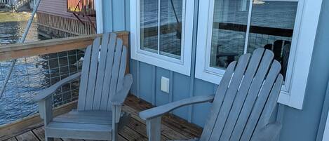 Una terraza de madera con dos sillas Adirondack, una barandilla y vista al agua.