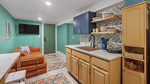 A compact kitchen with a sink, cabinets, and a countertop. There is a small dining area with a table and chairs. The walls are painted in two colors, and there is a patterned rug on the floor. - Cheerful Rainbow Suite • Near NYC (Jersey City)