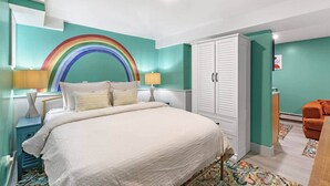 A bedroom with teal walls, a bed with a white bedspread, a rainbow mural, a white wardrobe, and an orange chair. - Cheerful Rainbow Suite • Near NYC (Jersey City)