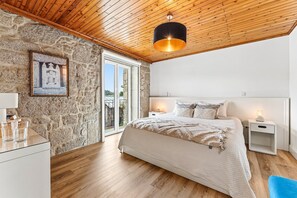 Ein Schlafzimmer mit Steinsandsteinwand, Holzboden und einem Bett mit weißem Kopfteil, Nachttischen und einer hängenden Deckenleuchte.