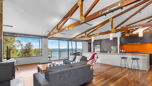A modern living room with a large grey sofa, a small table, and a bar area with stools. - Absolute Beachfront | 5BR Family Escape (Pindimar)