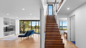 A modern interior with a wooden staircase leading to a balcony overlooking a body of water. - Absolute Beachfront | 5BR Family Escape (Pindimar)