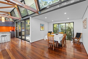 A modern kitchen with a large island, a dining area with a table and chairs, and a large sliding glass door leading to a patio. - Pindimar Beach Sanctuary – Absolute Beachfront (Pindimar)