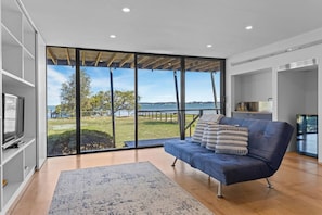 A modern living room with a large sliding glass door leading to a balcony with a view of the water and greenery. - Pindimar Beach Sanctuary – Absolute Beachfront (Pindimar)