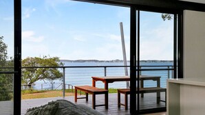 A room with a large window overlooking a body of water, wooden furniture, and a view of the landscape. - Absolute Beachfront | 5BR Family Escape (Pindimar)
