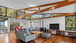 A spacious living room with a wooden ceiling, large windows, a grey sofa, a wooden coffee table, and a flat-screen TV. - Absolute Beachfront | 5BR Family Escape (Pindimar)