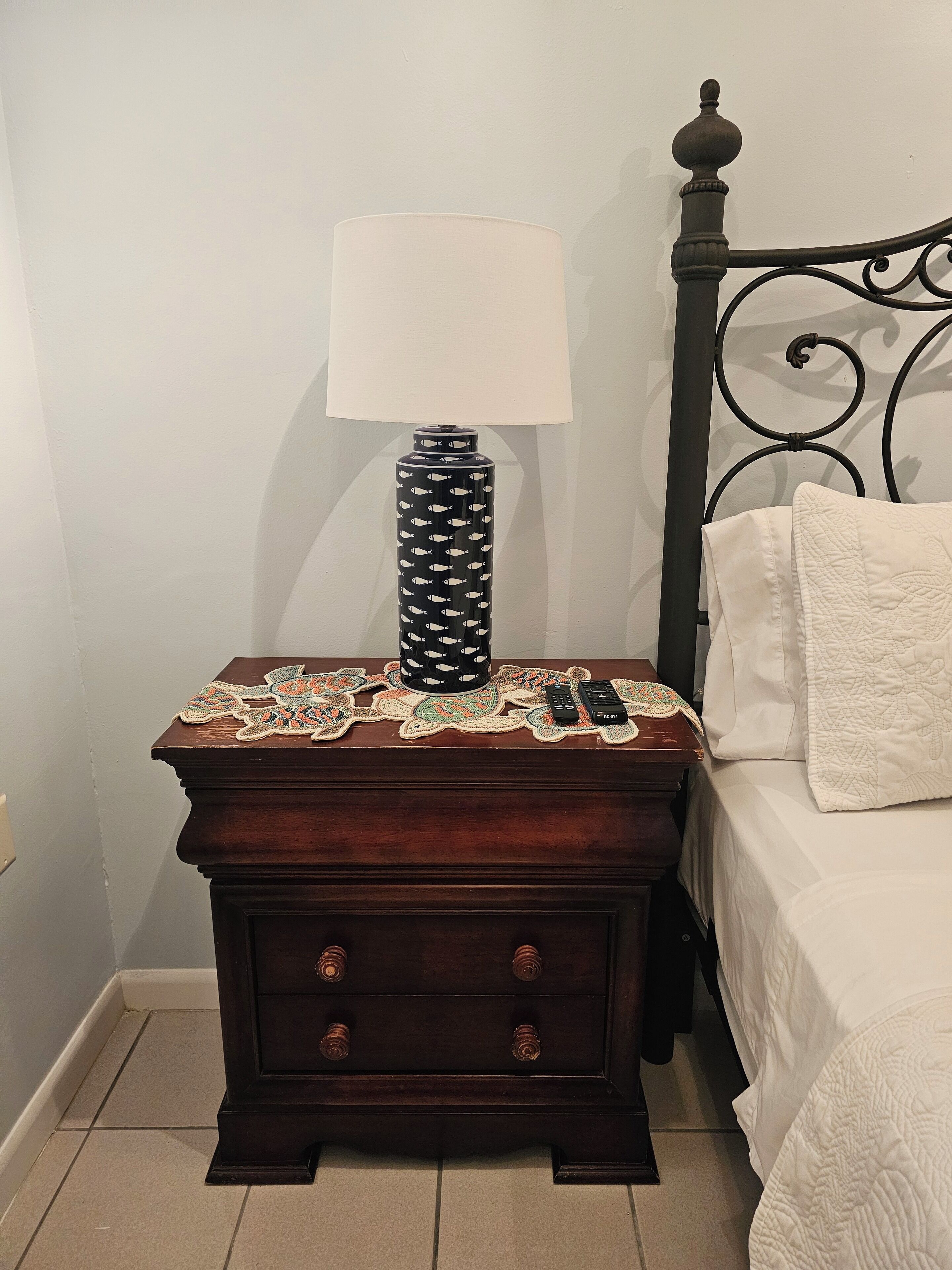 Une table de chevet en bois avec une lampe, une télécommande et un objet décoratif.