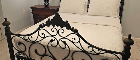 A bed with an ornate metal frame, a nightstand with a lamp, and a plain wall.