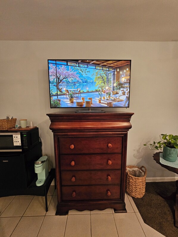 A television mounted on a wooden cabinet with a kitchen area visible below. - #3 Comfortable Private Room in Peaceful Sunrise Close to Shops and Dining (Sunrise)