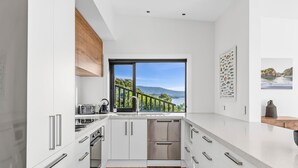 Eine moderne Küche mit weißen Schränken, Edelstahlgeräten und einem großen Fenster mit Blick auf Grünflächen und Berge.