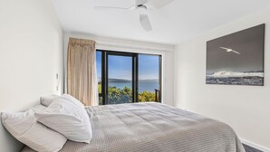 Ein Schlafzimmer mit einem Bett, einem Deckenventilator, einem großen Fenster mit Vorhängen und einem Gemälde einer Möwe.