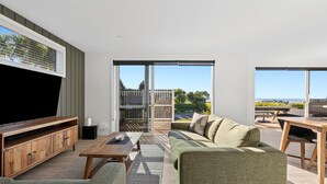 Una sala de estar moderna con un televisor de pantalla plana grande, un mueble de entretenimiento de madera, un sofá verde y un comedor con una mesa y sillas de madera.