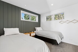 Une chambre avec deux lits, une table de chevet et deux fenêtres équipées de stores.
