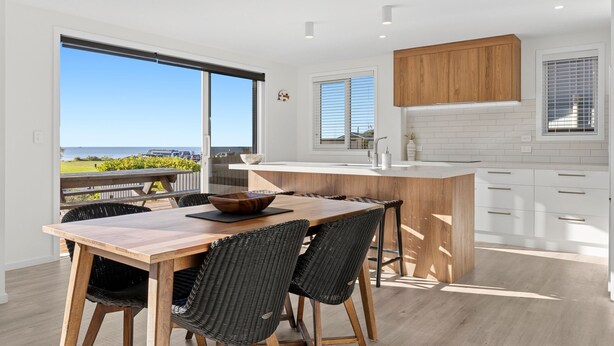 Una cocina moderna con una isla grande, armarios blancos y vista al océano.