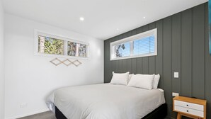 Un dormitorio con una cama, dos mesitas de noche y dos ventanas.