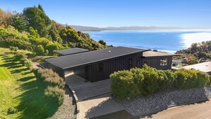 Ett modernt hus med ett platt tak, omgivet av frodig grönska och med utsikt över havet.
