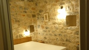Un dormitorio con estructura de cama de madera, pared de piedra y un cuadro enmarcado.