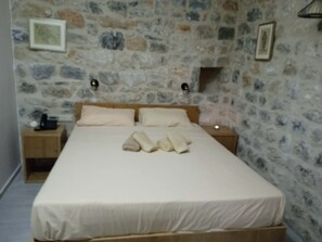 A bedroom with a stone wall, a wooden bed, two bedside tables, and a nightstand. - Torre Agetria Episkopē (Stavri)