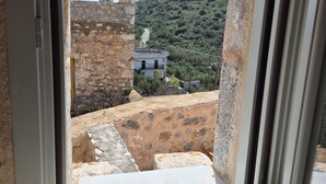 Una ventana con vistas a un muro de piedra y un edificio en una ladera.
