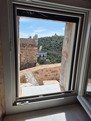 Ein Fenster mit Blick auf eine Steinmauer und ein Gebäude an einem Hang.