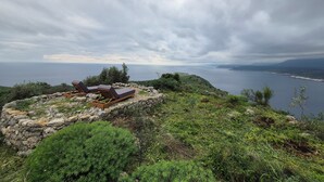 Un espacio al aire libre tranquilo con dos sillones de relax y una mesa de madera, con vistas a un paisaje costero y al mar, con colinas a lo lejos.