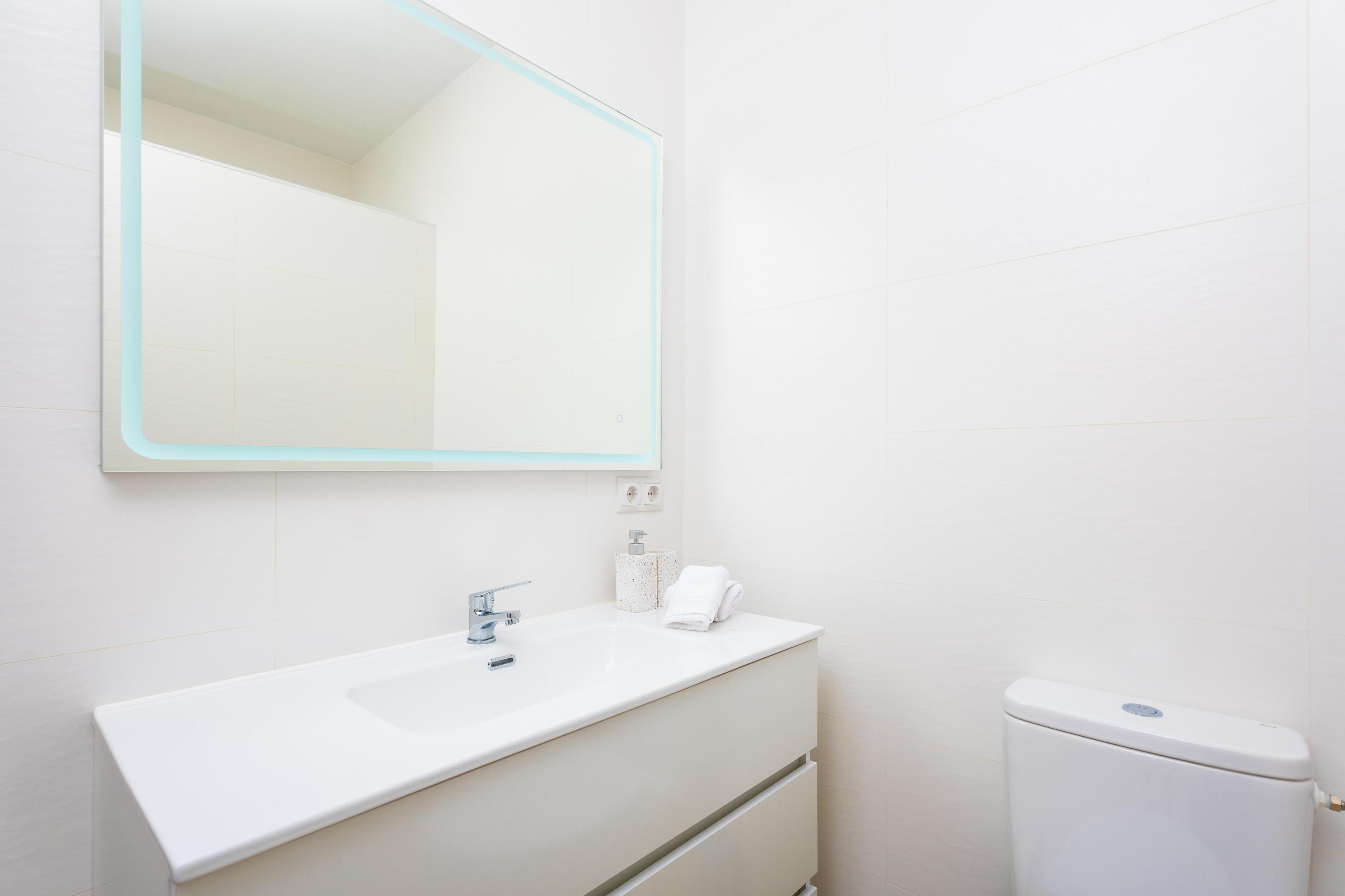 Un baño moderno con lavamanos, espejo y retrete blancos.