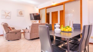 Uma sala de estar moderna com área de jantar, incluindo um sofá, poltrona reclinável e uma mesa com uma fruteira.