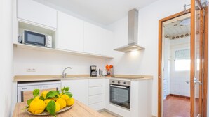 Uma cozinha moderna com armários brancos, uma mesa de madeira com limões, um micro-ondas, uma cafeteira e um forno.
