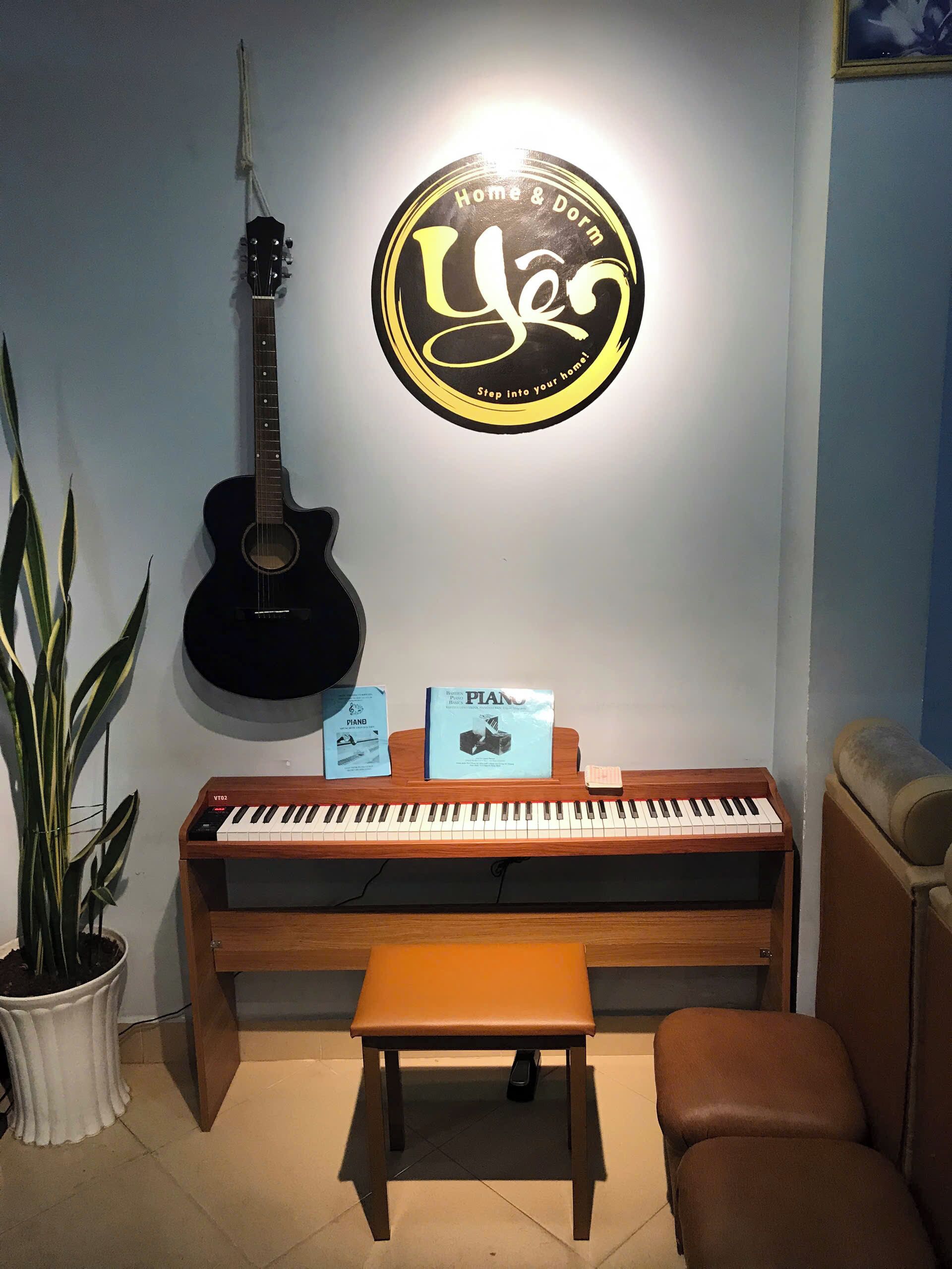 A room with a piano, a guitar, a plant, and a wall decoration.