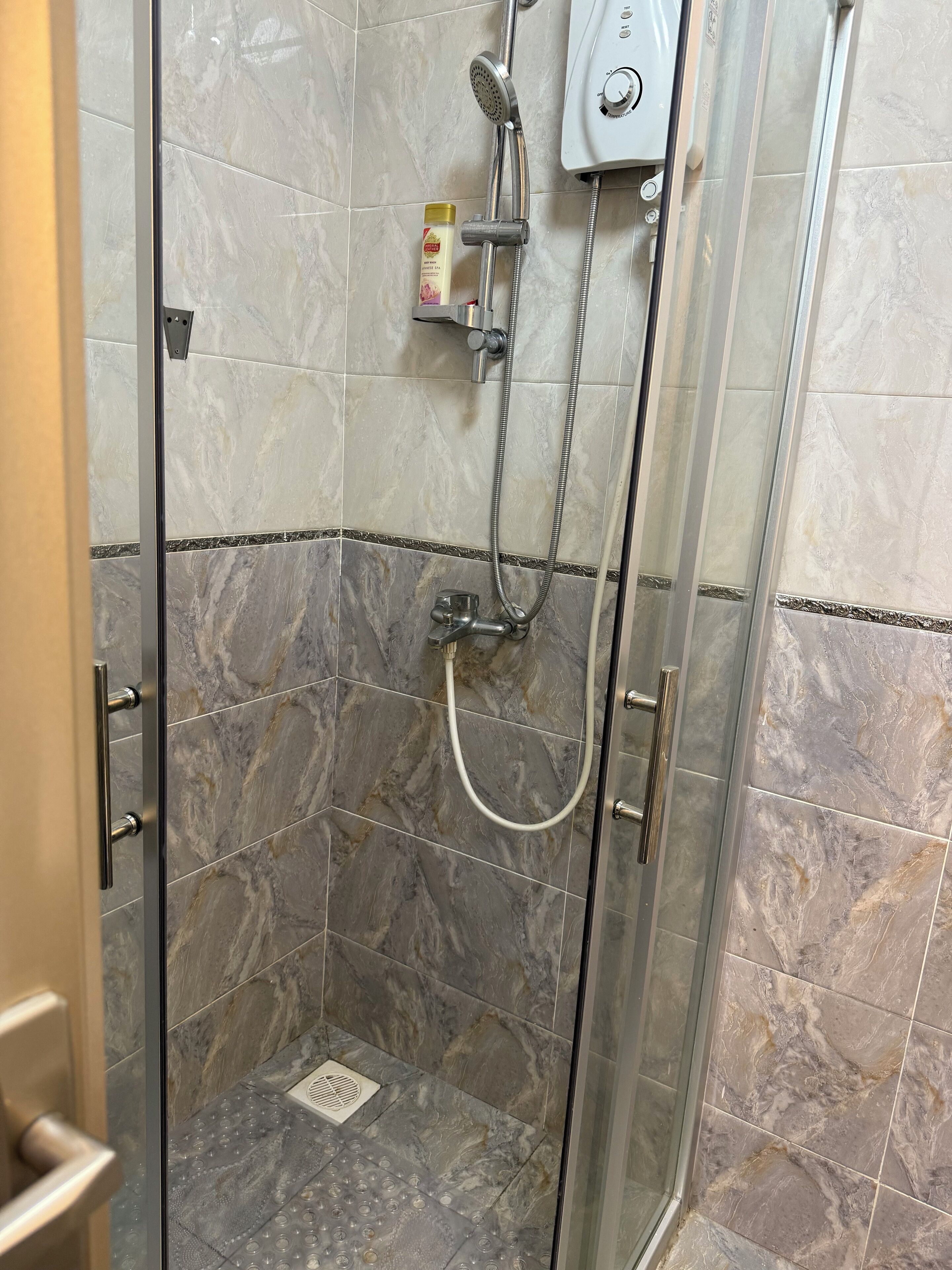 Et brusebad med glasvægge, et håndholdt brusehoved og et kontrolpanel på væggen.
