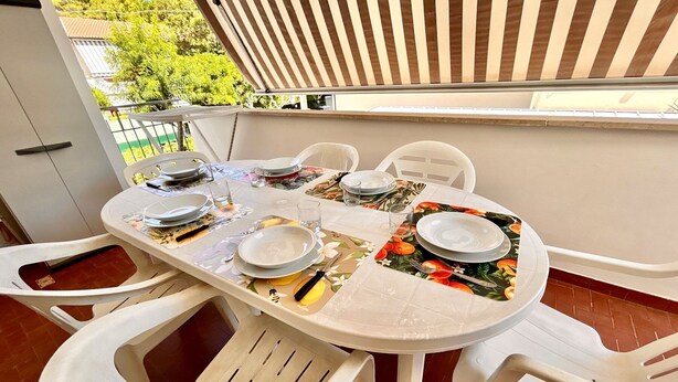 Een ronde eettafel met witte stoelen, gedekt met borden, glazen en bestek.