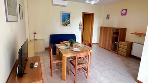 A dining area with a wooden table and chairs, a television on a stand, and a ceiling fan. - Bilo onda, near the sea and downtown with a/c (Numana)