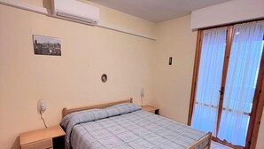 A bedroom with a single bed, bedside tables, a ceiling light, an air conditioning unit, a window with curtains, and a small picture on the wall. - Bilo onda, near the sea and downtown with a/c (Numana)