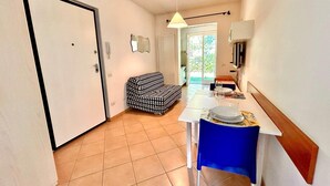 A compact living space with a kitchenette, a dining table with chairs, a patterned sofa, and a sliding glass door leading to an outdoor area. - Two-room apartment Leonardo - Sirolo (Sirolo)