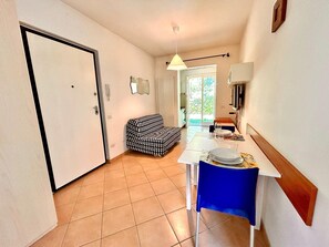 A compact living space with a kitchenette, a dining table with chairs, a patterned sofa, and a sliding glass door leading to an outdoor area. - Two-room apartment Leonardo - Sirolo (Sirolo)