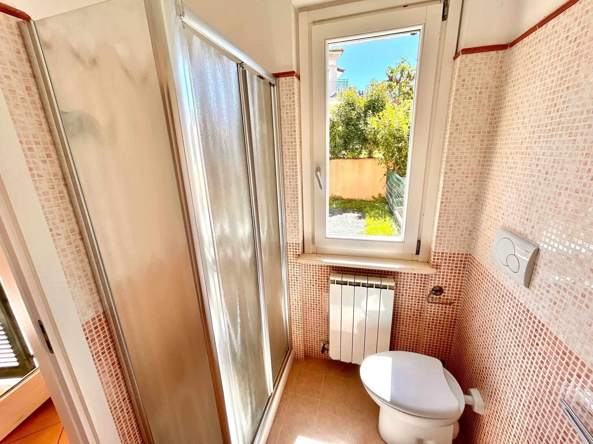 A compact bathroom with a toilet, a window, and a radiator.