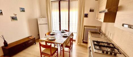 A compact kitchen with a gas stove, a dining table set for four, and a refrigerator.