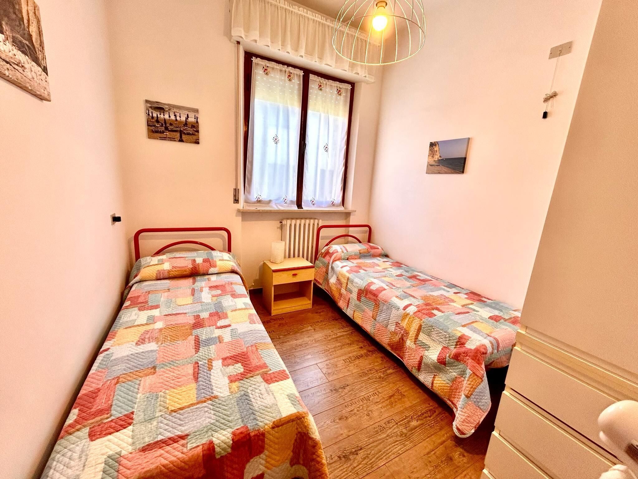 Ein kleines Schlafzimmer mit zwei Einzelbetten, einem Holznachttisch, einem Heizkörper und einem Fenster mit Vorhängen.