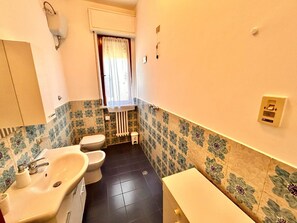 A small bathroom with a toilet, sink, and a window with a curtain. - Trilo Ilario in Sirolo, with wifi and parking (Sirolo)