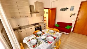 Un espacio habitable compacto con cocina, comedor y un sofá rojo con cojines verdes.