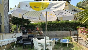 An outdoor seating area with a table and chairs under a large umbrella, surrounded by greenery and a stone wall. - Two-room apartment Leonello with garden and a/c (Numana)