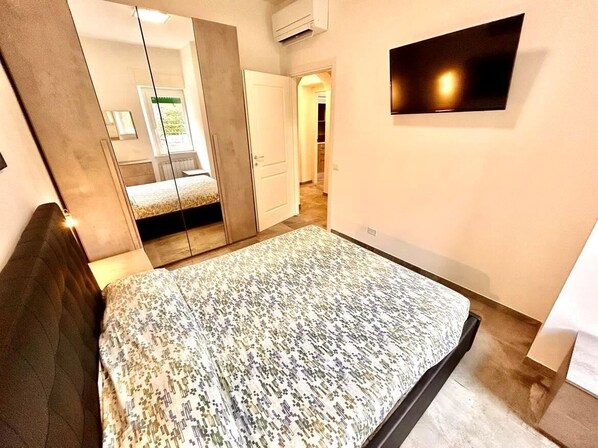 A bedroom with a bed, a wardrobe, a mirror, and a TV on the wall. - Two-room apartment Leonello with garden and a/c (Numana)