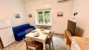 A compact kitchen with a dining table, blue sofa, and a TV. - Two-room apartment Leonello with garden and a/c (Numana)