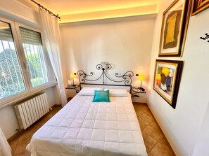A neatly made bed with a white duvet, a teal pillow, and two bedside lamps.