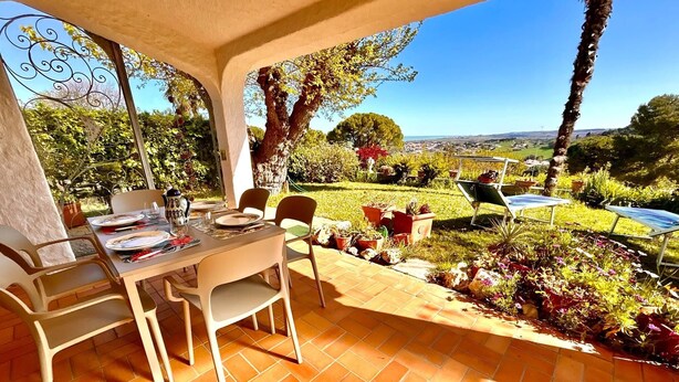 A patio with a table set for two, surrounded by potted plants and a view of a lush garden. - Villa Margherita, with garden, sea view and wifi (Numana)