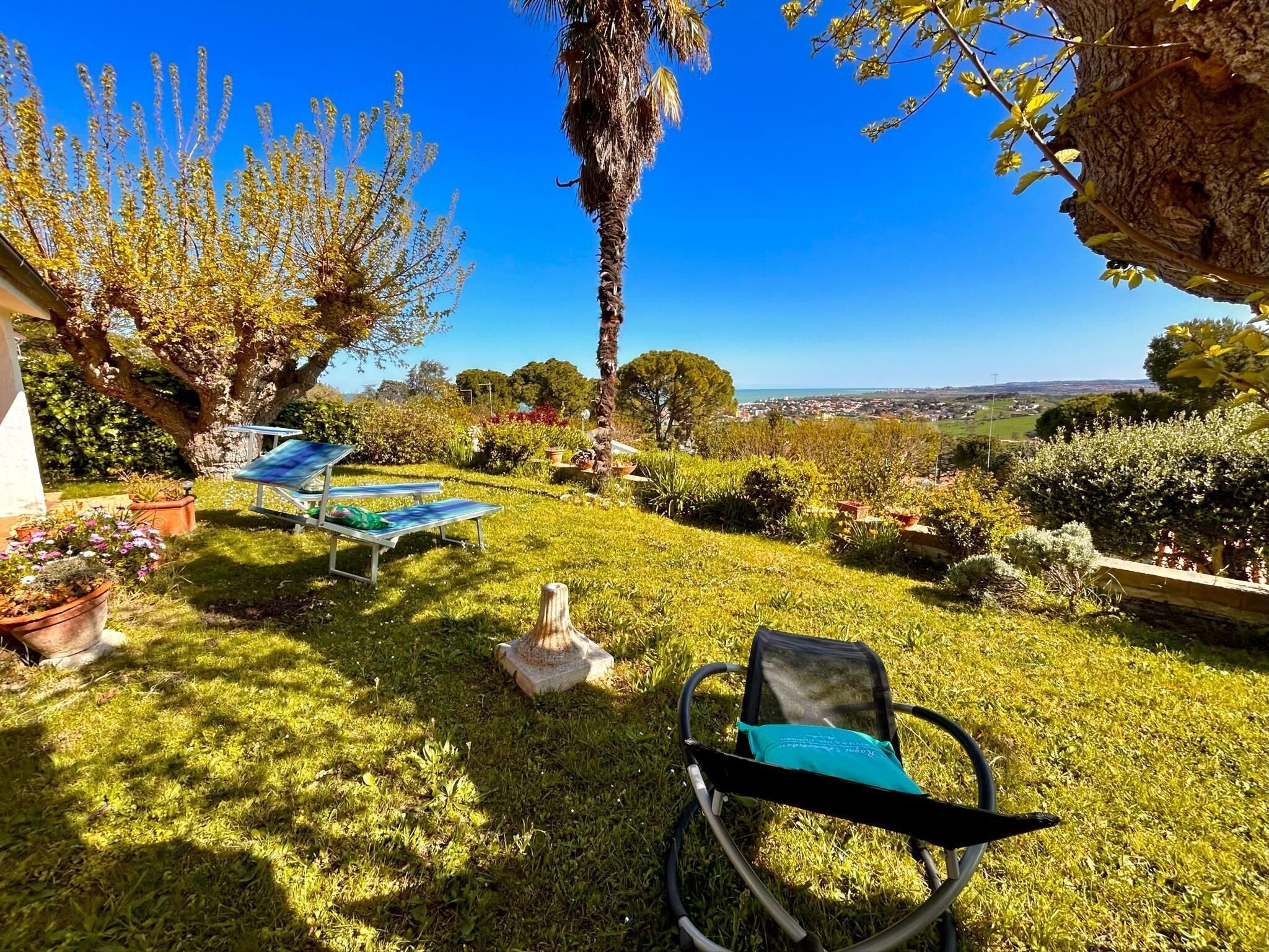 Ein Garten mit Rasen, einer Steinfigur und Blick auf eine Stadt in der Ferne.