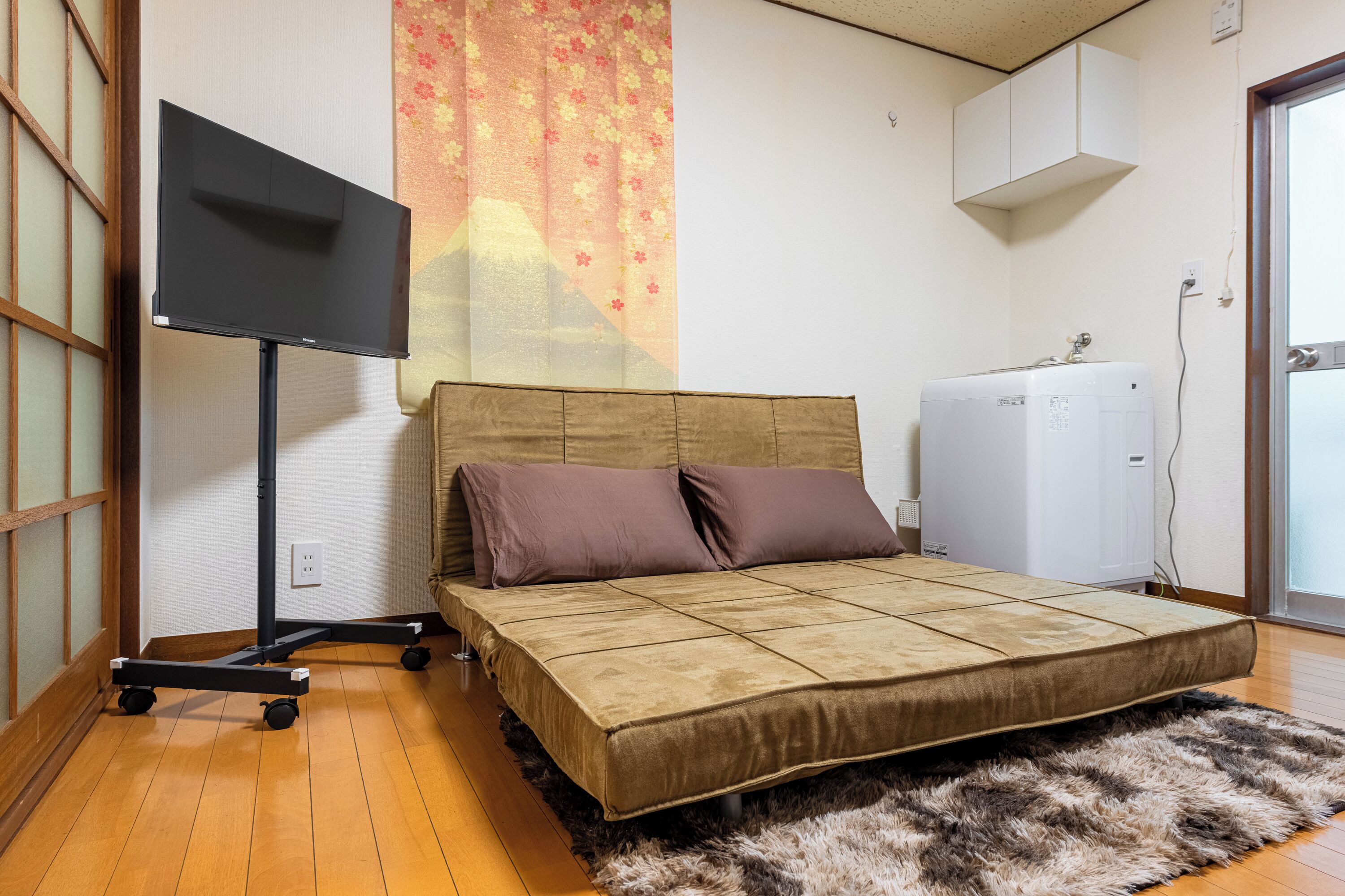 Ein Zimmer mit einem Bett, einem Fernseher auf einem Schrank, einem Heizkörper und einem Fenster.