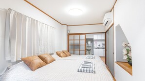 Ein Hotelzimmer mit einem großen Bett, einem hölzernen Kopfteil, einer kleinen Küchenzeile und einem durch eine Schiebetür einsehbaren Badezimmer.
